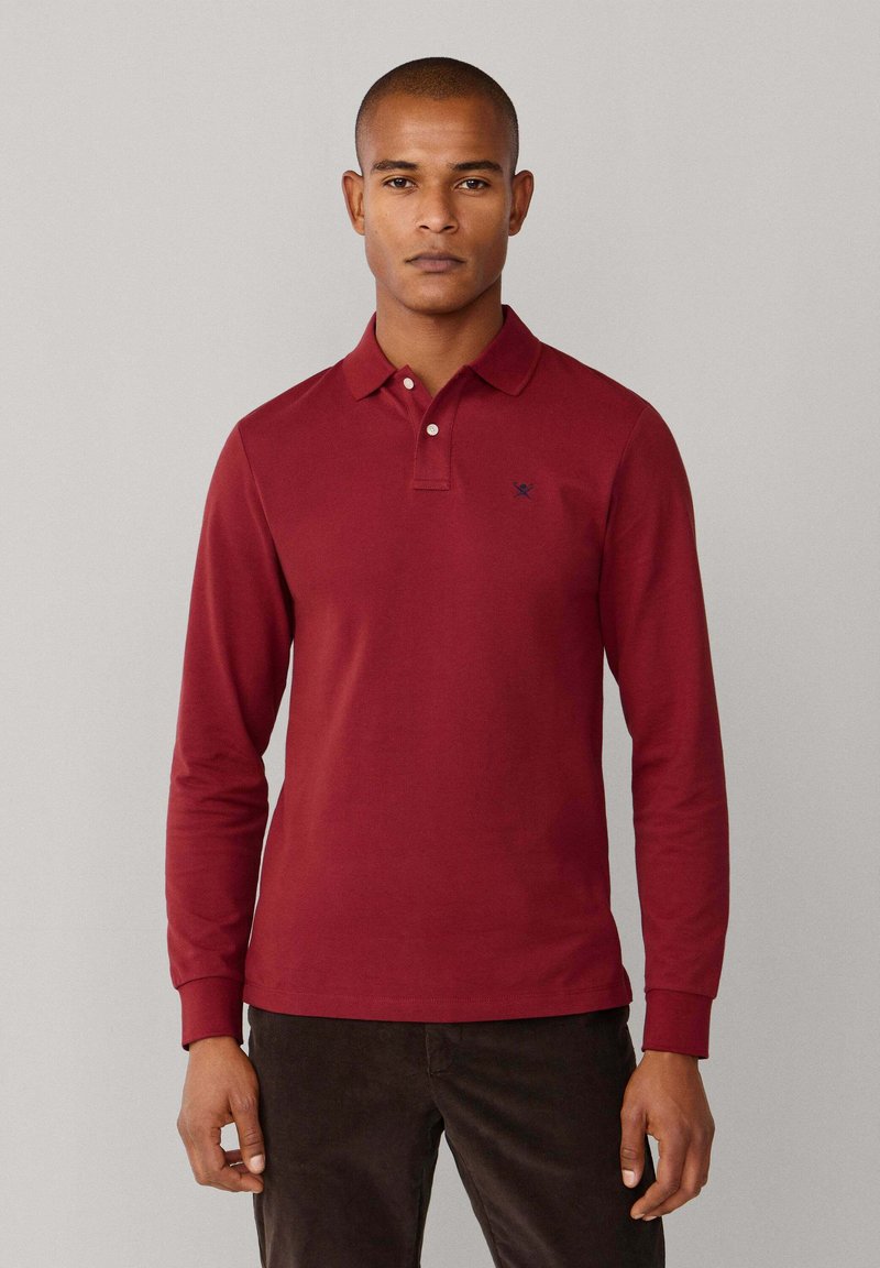 Polo à manches longues en coton rouge profond avec col et patte à trois boutons. Présente un petit logo bleu marine sur la poitrine.