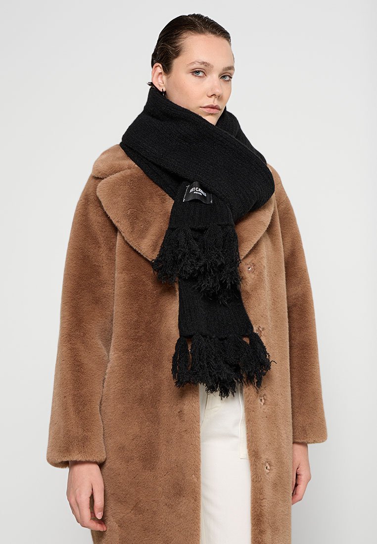 Sciarpa nera con frange realizzata in tessuto testurizzato, indossata sopra un cappotto di pelliccia marrone. La sciarpa è annodata in modo rilassato attorno al collo.