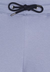 Nära bild av ljuslila stickad tyg med en svart dragsko knuten i en rosett genom silverfärgade öglor vid midjan.