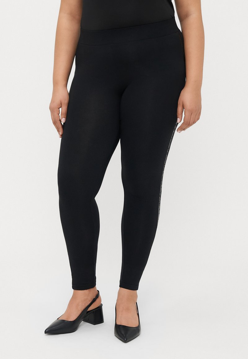 Μαύρα κολάν με ψηλή μέση, λεία υφή και πλαϊνές λεπτομέρειες που διαθέτουν μια διακριτική μεταλλική πινελιά. Συνδυασμένα με μαύρα παπούτσια με τετράγωνο τακούνι.