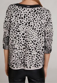 Szary sweter z czarnym wzorem w kropki, paskowymi mankietami w czerni i bieli oraz luźnym krojem z okrągłym dekoltem.