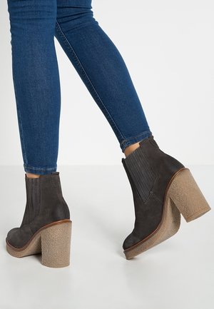 Bottes de cheville gris foncé en suède, avec des panneaux latéraux en élastique, un talon épais beige texturé et des bordures marron contrastantes.