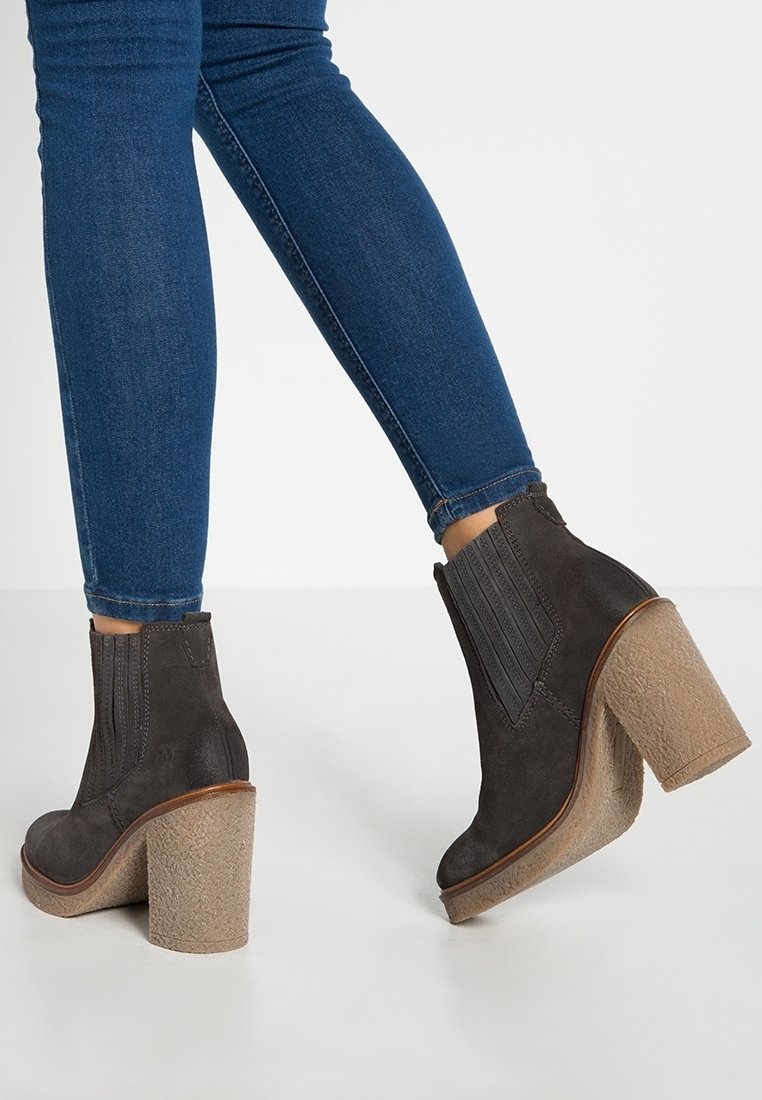 Tummanharmaat nilkkurit, jotka on valmistettu mokasta, varustettu joustavilla sivupaneeleilla, paksulla beigellä tekstuurilla varustetulla korkolla ja kontrastoivalla ruskealla reunuksella.