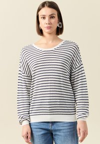 Gestreepte witte en marineblauwe trui met een ronde halslijn, lange mouwen en een ribgebreide onderkant. Kenmerkt zich door een textuur, opengehaakt patroon.