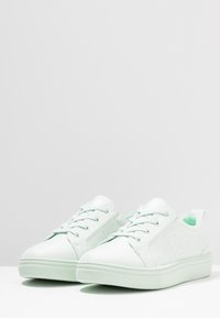 Jasnozielone sneakersy wykonane z gładkiego materiału, z systemem sznurowania, teksturowaną gumową podeszwą i perforowanymi akcentami po bokach.