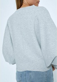 Hellgrauer Pullover mit strukturiertem Finish, oversized Ärmeln und rundem Halsausschnitt, von hinten gezeigt.