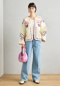 Quiltet kremfarget jakke med rosa og lilla mønster, med rund hals og to lommer, kombinert med høy midje lys denim og en rosa veske.
