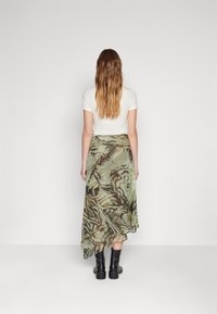 Fustă fluidă, cu un pattern verde și maro, având un tiv asimetric, purtată cu un tricou alb și botine negre până la gleznă.