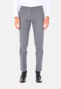 Pantaloni grigi slim-fit realizzati in un mix di cotone con una texture liscia. Presentano una chiusura frontale con bottone e tasche laterali. Indossati con scarpe nere.