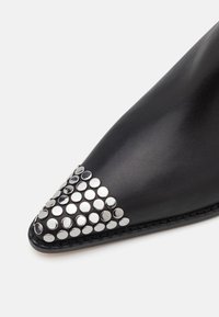 Scarpa in pelle nera con punta affusolata, decorata con borchie argentate disposte in un gradiente sulla punta. Finitura testurizzata.