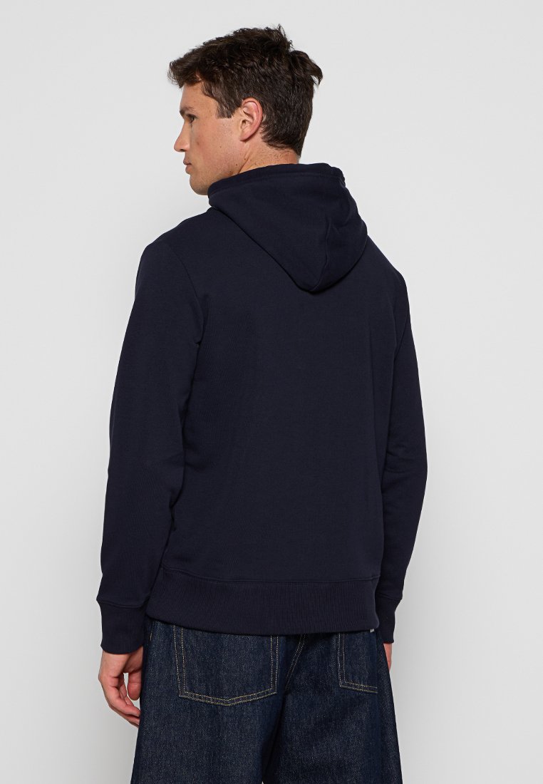Un sweat à capuche bleu marine présente une texture côtelée, une poche kangourou et une taille ajustée, fabriqué à partir d'un tissu doux et léger.