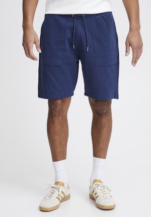 Marineblå shorts lavet af tekstureret stof, der har en snor i taljen, to frontlommer og en behagelig pasform. Sammen med hvide sokker og sneakers.