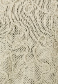 Maglione lavorato a maglia crema con motivi texturizzati e ondulati sulla superficie. Presenta un design a punto aperto e morbido che conferisce un aspetto soffice.