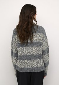 Pelēks adīts džemperis ar krēmkrāsas ģeometrisko rakstu, ar brīvu piegriezumu, garām piedurknēm un strukturētu auduma apdari.