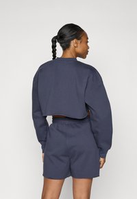 Mørkeblå cropped sweatshirt med lange ærmer og rund hals, kombinert med matchende shorts, laget av et mykt, teksturert materiale.