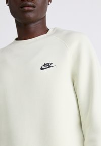 Ljusgul Nike sweatshirt med rund halsringning, ribbstickade muddar och en svart logotyp på vänster bröst. Mjuk tyg med en slät textur.