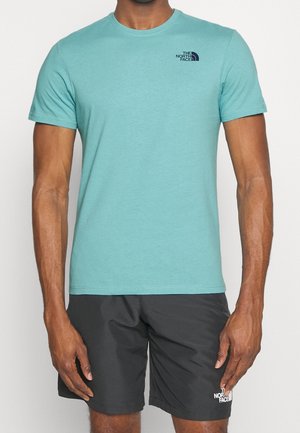 Mand iført en lyseblå t-shirt med korte ærmer og sorte shorts, begge med The North Face-logo.