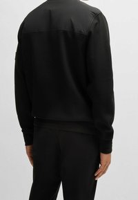 Mustapaita, jossa on teksturoitu, ribattu alaosa ja sileä yläpaneeli. Pitkät hihat, joissa on hihansuut, vähäinen brändäys.