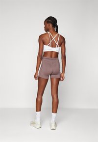 Top sportivo bianco con spalline incrociate, abbinato a pantaloni corti marroni, caratterizzato da una texture liscia e un design aderente per il comfort.