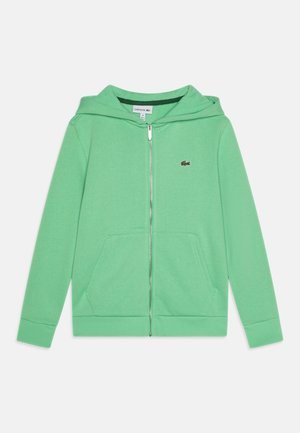 Sudadera con capucha verde con cremallera, hecha de tela suave, que cuenta con una cremallera frontal, dos bolsillos laterales y un pequeño logo de Lacoste en el pecho izquierdo.