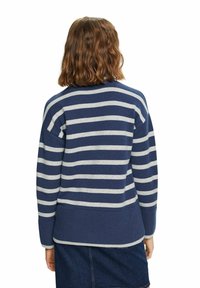 Personne aux cheveux bruns mi-longs portant un pull rayé bleu et blanc et une jupe bleu foncé, vue de dos.