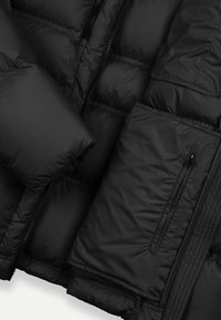 Jachetă puffer neagră cu un design matlasat, buzunare cu fermoar și o textură netedă, lucioasă. Panouri multiple izolante pentru căldură.