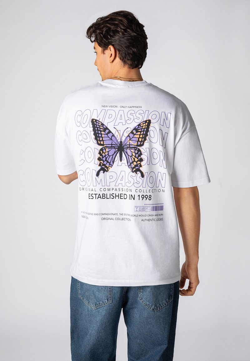 Weißes Baumwoll-T-Shirt mit einem großen lila-schwarzen Schmetterlingsmotiv auf der Rückseite, mit Text und Details in Lila, Grau und Schwarz.