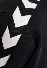 Fekete szövet, textúrált felszínnel, amelyen egy fehér cikkcakk minta található az egyik oldalon. Nincs más figyelemre méltó részlet.
