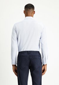  Lichtblauwe lange mouwen blouse met een textuurafwerking en knoopmanchetten, gecombineerd met donkerblauwe broeken met een elastische tailleband en achterzakken.