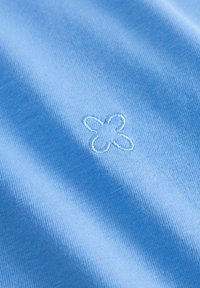 Lichtblauwe stof met een zachte textuur, versierd met een klein, geborduurd bloemenpatroon. De stitching is subtiel en licht verhoogd.