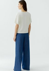 Lässiges, kurzärmeliges Cremeoberteil, kombiniert mit weit geschnittenen, blauen Jeans. Sanfte Textur mit subtiler Drapierung. Einfaches und minimalistisches Design.