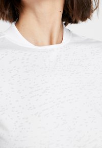 Vit t-shirt med ett subtilt strukturerat mönster, med rundad halsringning och ett mjukt, lätt material.