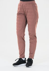 Roze, gevoerde broek met een elastische tailleband, zijzakken en ritsen bij de enkels, gecombineerd met zwarte sport schoenen.