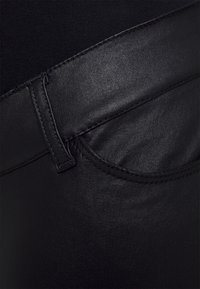 Jeans negros elásticos que presentan un bolsillo delantero, textura suave y detalles de costura en la cintura y los bordes del bolsillo.