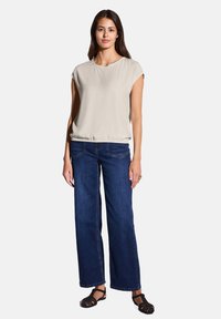 Blusa corta a maniche corte color beige chiaro con vita arricciata, abbinata a jeans a gamba larga blu scuro e sandali intrecciati neri.