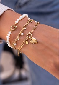 Pulsera de cadena de oro con perlas blancas, encanto en forma de corazón con acentos de perla y pequeños encantos redondos adicionales; diseño en capas.