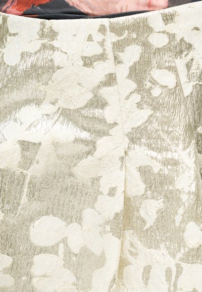 Metalinis auksinis audinys su gėlių raštu elnių spalva, reljefine struktūra ir subtiliu blizgesiu, rodantis siūlės detalę.