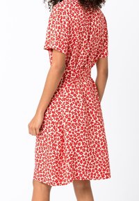 Czerwona i biała sukienka w wzory, z krótkimi rękawami, podkreśloną talią i spódnicą do kolan; materiał pokryty kwiatowym wzorem.