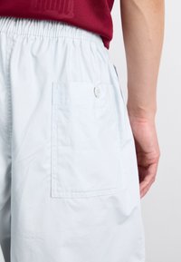 Világoskék short, rugalmas derékkal, hátul gombos zsebbel és sima textúrával. Minimalista dizájn.