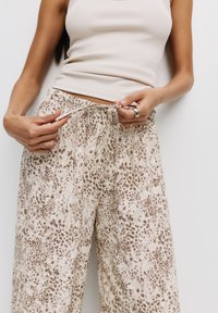 Pantalons larges à imprimé léopard en beige clair et marron, avec une taille élastique dotée d'un cordon de serrage. Tissu doux et texturé.