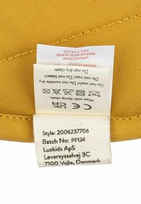 Žltá látka s hladkou textúrou obsahuje štítok na starostlivosť. Štítok obsahuje pokyny na starostlivosť a údaje o produkte čiernym textom na bielom pozadí.