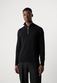 Zwarte zip-up trui gemaakt van zacht materiaal, met een hoge kraag, geborduurd logo, en geribbelde manchetten en zoom voor een aangesloten look.