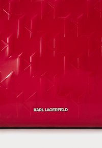 Pochette rouge gaufrée avec un motif géométrique et un logo argenté "KARL LAGERFELD" en bas. Texture lisse et brillante.