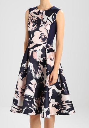 Robe bleu marine sans manches avec un grand imprimé floral rose clair et blanc, corsage ajusté et jupe évasée longueur genou.