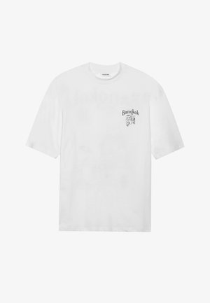 Camiseta de algodón blanca con un corte oversize, que presenta un gráfico negro de un tuk-tuk y el texto "Bangkok" en la zona izquierda del pecho.