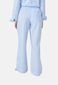 Pantalones de rayas finas en azul claro, con un corte relajado, cinturilla elástica y pequeño bolsillo trasero; la tela parece suave con un ligero brillo.