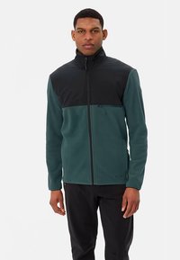 Fleecejack met hoge kraag, uitgevoerd in een teal kleurig lijfje en zwarte bovenkant. Voorzien van een zak met ritssluiting aan de voorkant, een gladde textuur en contrasterende kleurvlakken.