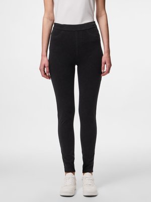 Leggings negras con cintura alta, fabricadas con un material suave y elástico, que presentan un corte ajustado y hasta los tobillos, combinadas con zapatillas blancas.
