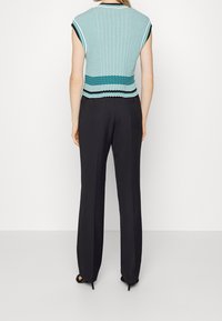 Jasnoniebieski sweter z ciemnym wykończeniem, z prążkowaną fakturą i falistym wzorem. Połączony z czarnymi, szerokimi spodniami.