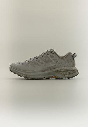 Siva tekaška čevelj za trail tek z teksturiranim podplatom, zgornjim delom iz mrežice, vezalkami in logotipom Vibram na strani, prikazan v stranski profil na nevtralnem ozadju.